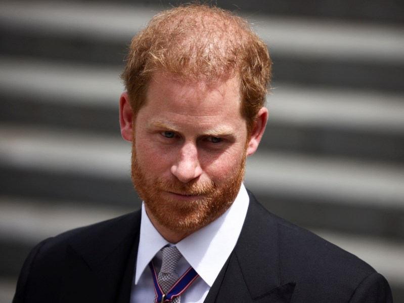 close up of Prince Harry in a black suit and white shirt with tan tie