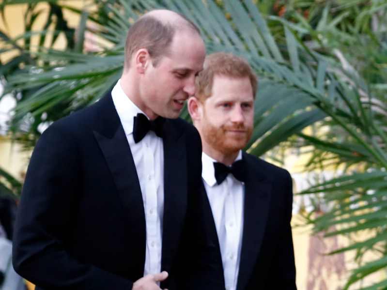 Prince William (L) and Prince Harry, both wearing black suits with black bowties and looking ahead as they walk