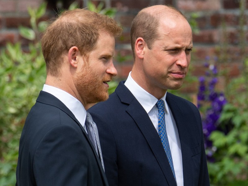 Prince Harry (L) and Prince William looking on while wearing deep navy blazer suits
