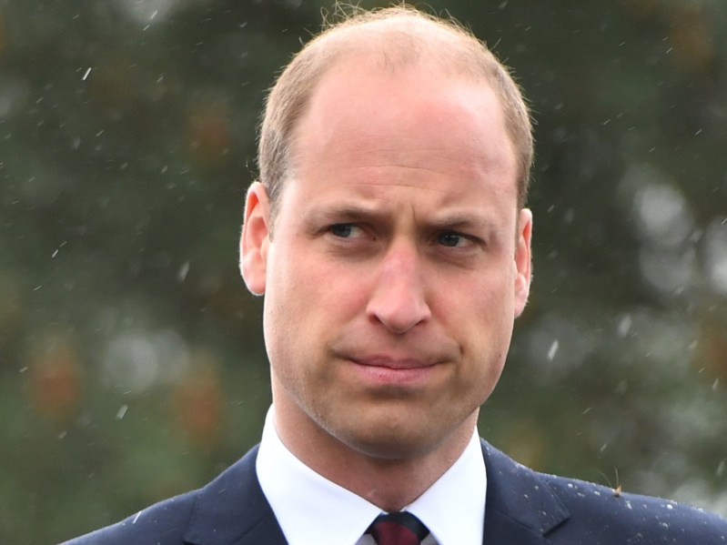 Prince William wears a dark suit at an outdoor royal event in the rain