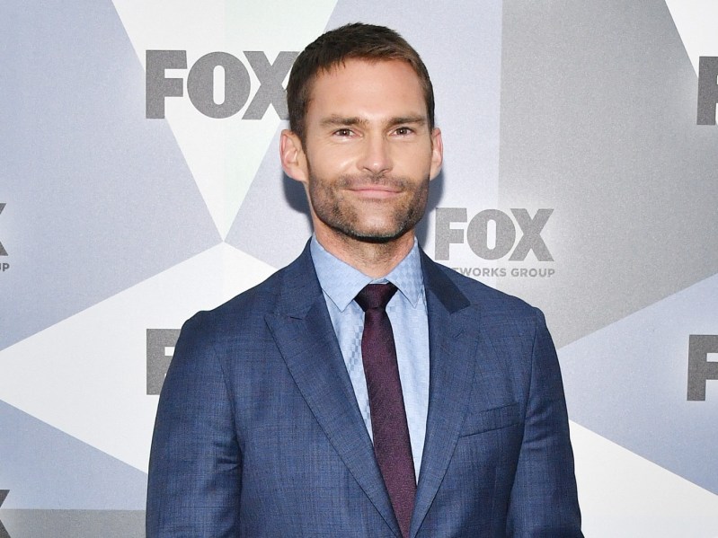 Seann William Scott smiles while wearing a blue blazer over a gray shirt and burgundy tie.
