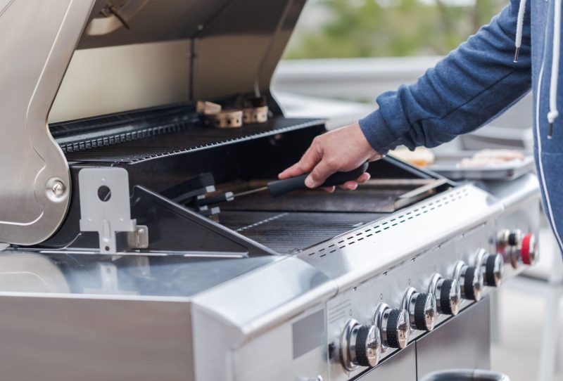 A large gas grill being cleaned with a grill brush
