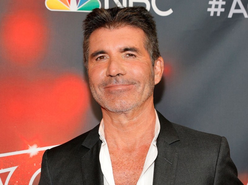 Simon Cowell smiles while wearing a white dress shirt and black blazer