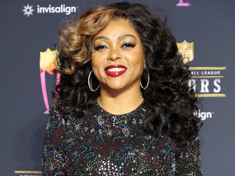 Taraji P. Henson smiles while wearing hoop earrings, red lipstick, and a patterned dress