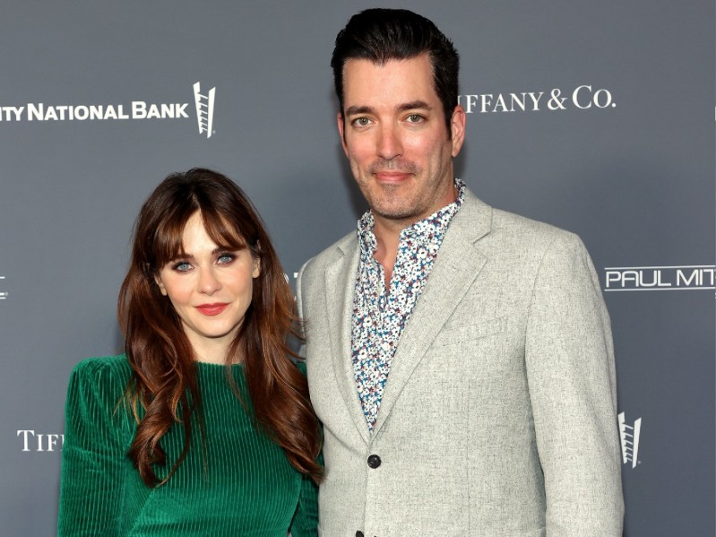 Zooey Deschanel wears a green dress and stands next to Jonathan Scott, in a beige suit, on the red carpet
