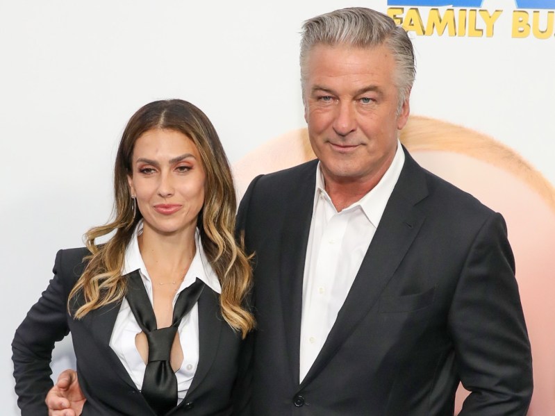Hilaria Baldwin (L) dressed in suit and loose tie standing next to Alec Baldwin, dressed in white dress shirt and black blazer
