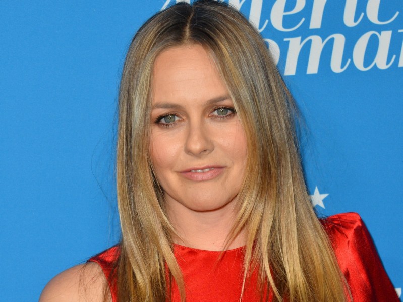 Closeup of Alicia Silverstone wearing red dress against blue backdrop