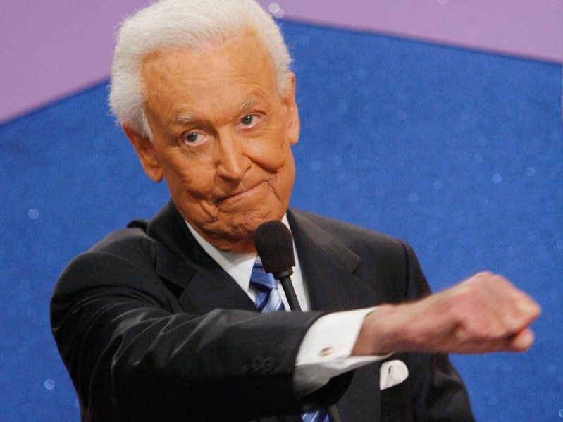 Bob Barker holds a microphone in one hand and makes a fist with the other on the set of The Price Is Right