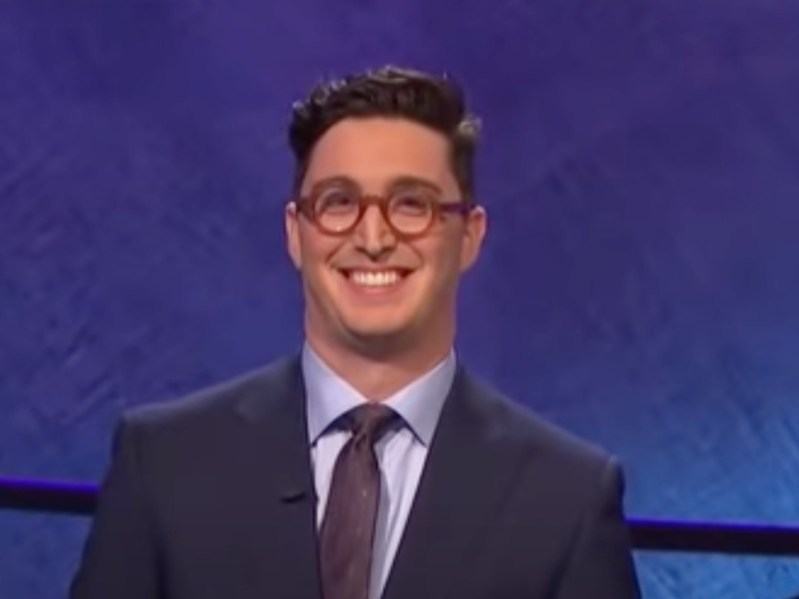 Buzzy Cohen smiles in suit against dark blue backdrop