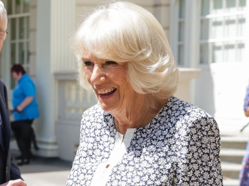 Camilla Parker Bowles laughs while wearing white top with blue pattern