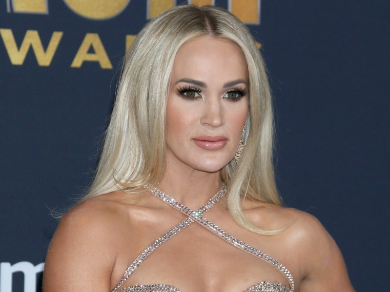 Carrie Underwood looks ahead while wearing strappy silver dress against navy blue background