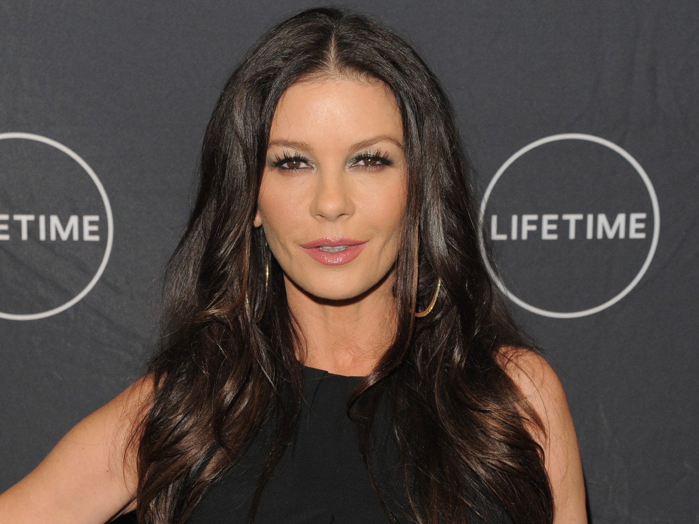 Catherine Zeta-Jones smiles in black dress against black background