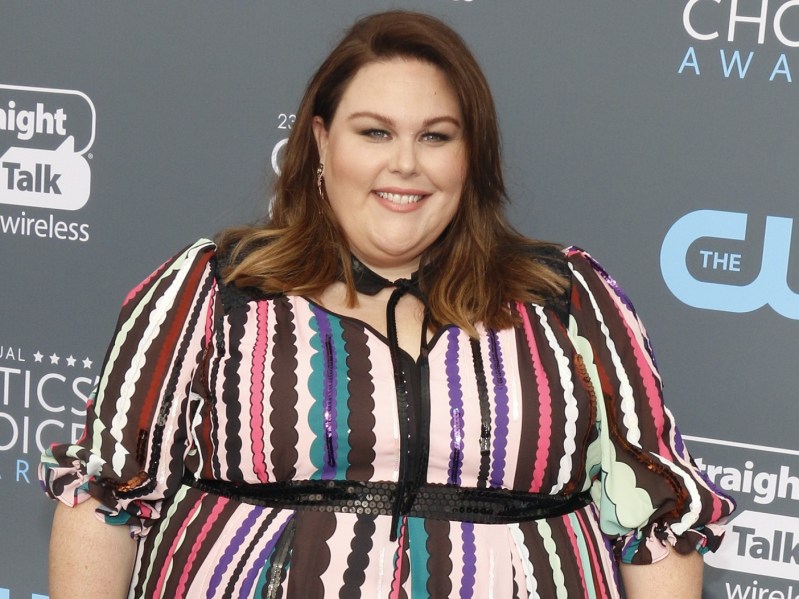 Chrissy Metz smiles against gray backdrop while wearing multicolored striped dress