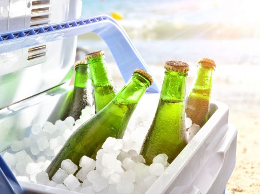 Bottles of beer chilled on ice in an ice chest/cooler on a beach