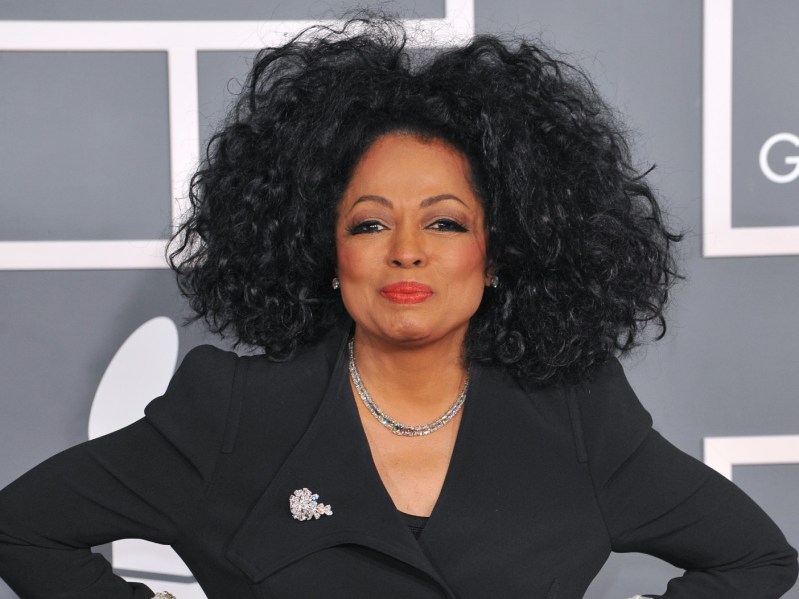 Diana Ross looks ahead with a smirk while wearing a black blazer and her hair styled in an afro