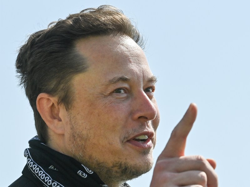 Closeup of Elon Musk with his finger pointing to the sky.