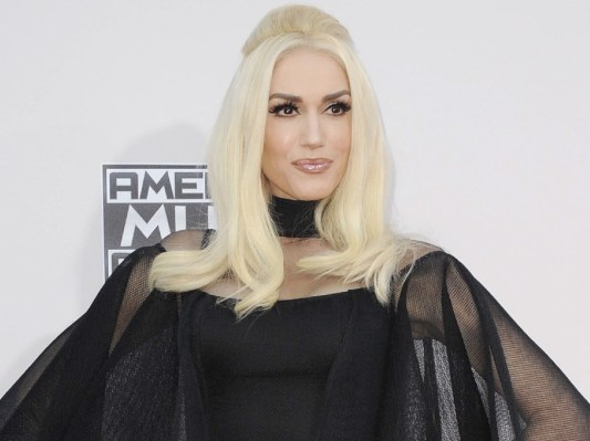 Gwen Stefani smiles while wearing black dress with black cloak over top