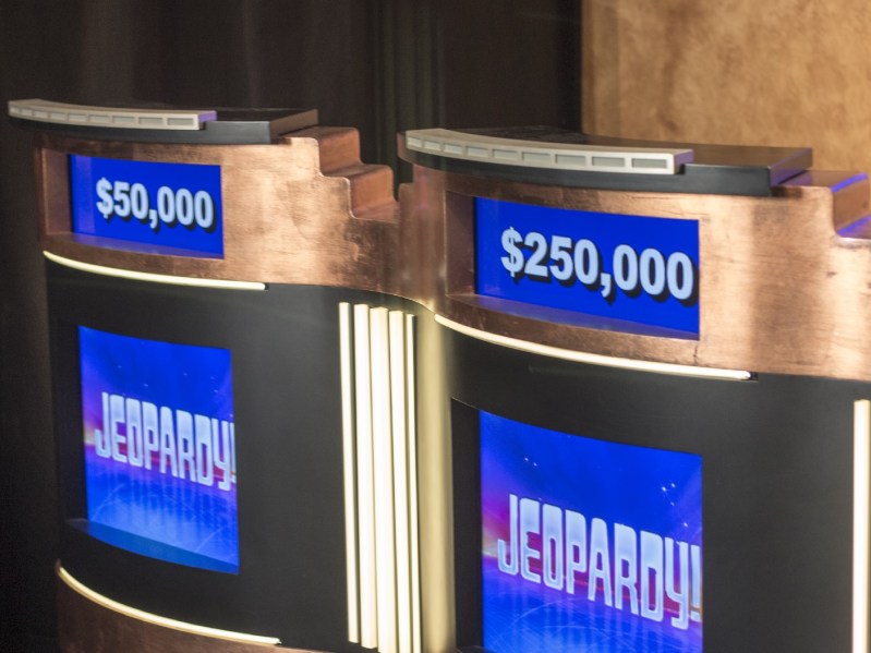 Two "Jeopardy!" podiums stand empty with different dollar amounts displayed on the screen