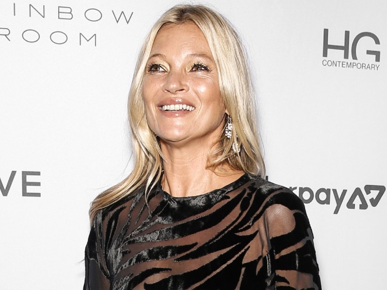 Kate Moss smiles while wearing black dress against white background