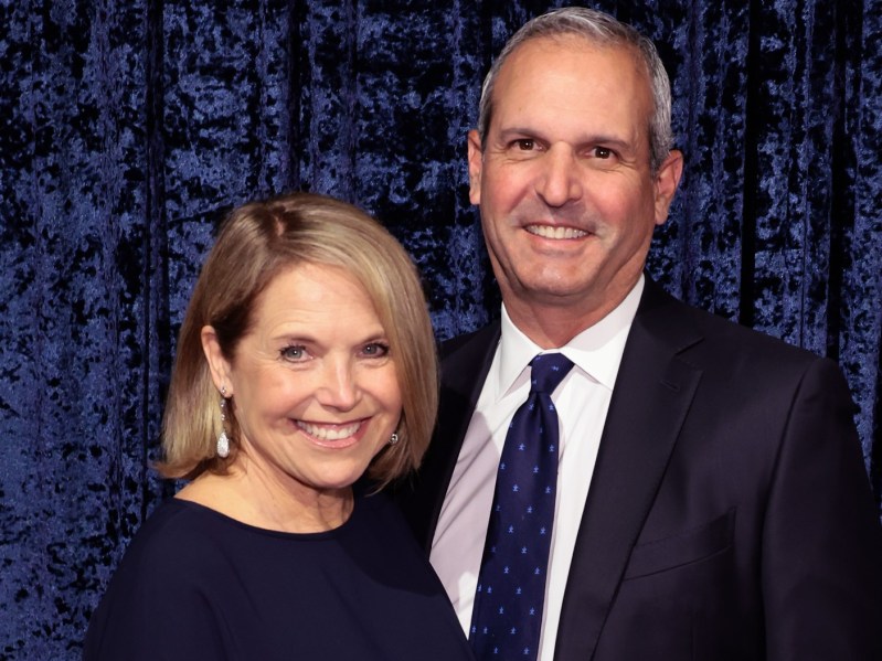Katie Couric (L) in dark navy blue dress standing next to John Molner, who is wearing a classic black suit with deep navy tie
