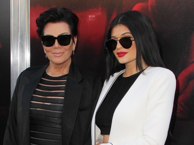Kris Jenner (L) wearing black outfit and sunglasses standing next to Kylie Jenner, who is wearing sunglasses, a black crop top, and a white jacket