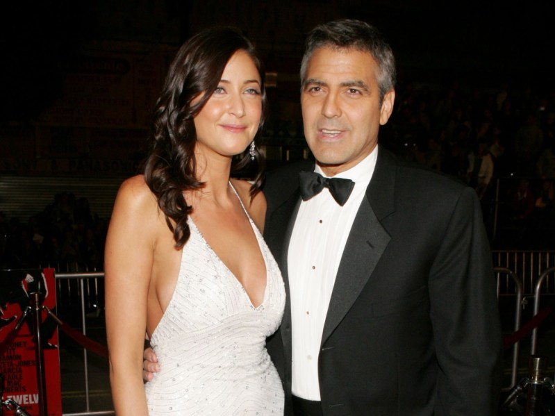 Lisa Snowdon (L) wearing white gown standing next to George Clooney, who is wearing a classic black suit and bowtie. They are standing against a black background