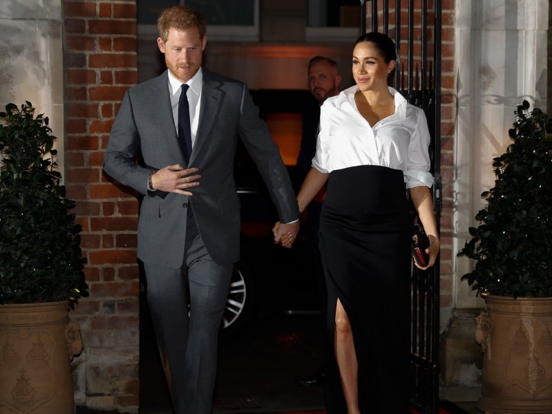 Prince Harry, in a gray suit, walks with wife Meghan Markle, in a white and black dress