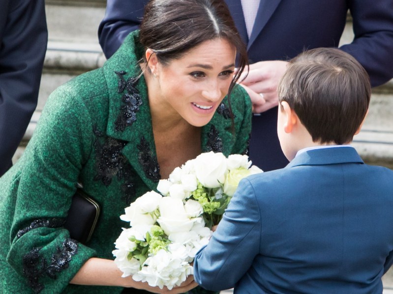 Meghan Markle, wearing a green coat, accepts flowers from a young boy during a royal event