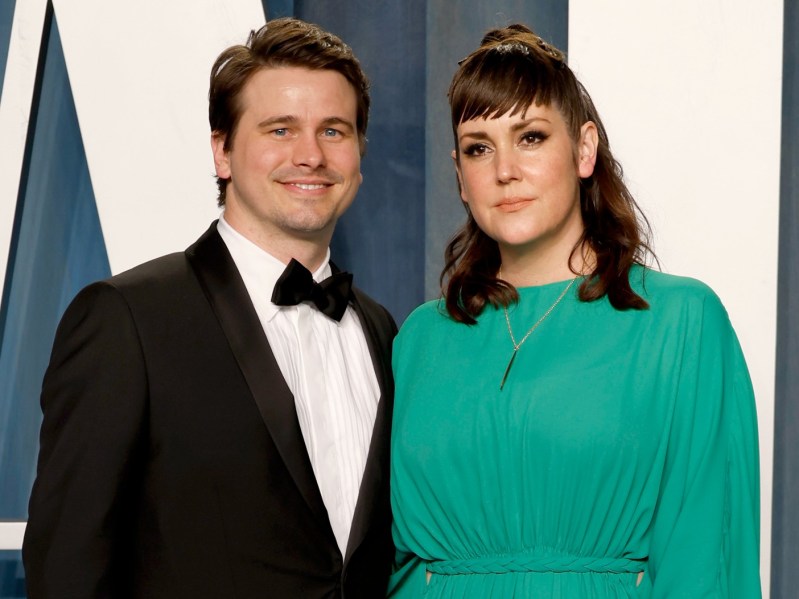 Melanie Lynskey (R) wearing kelly green smock dress, standing next to Jason Ritter, who is wearing a classic black suit and matching bowtie