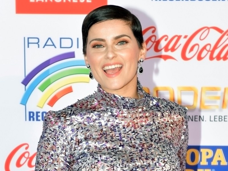 Nelly Furtado smiles in silver jumpsuit against colorful backdrop
