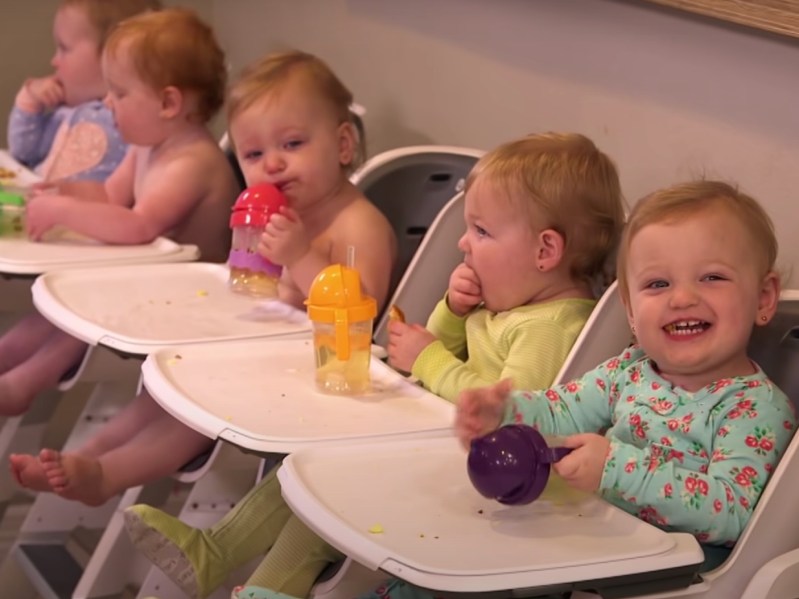 Five babies sit in high chairs side by side and sip from sippy cups