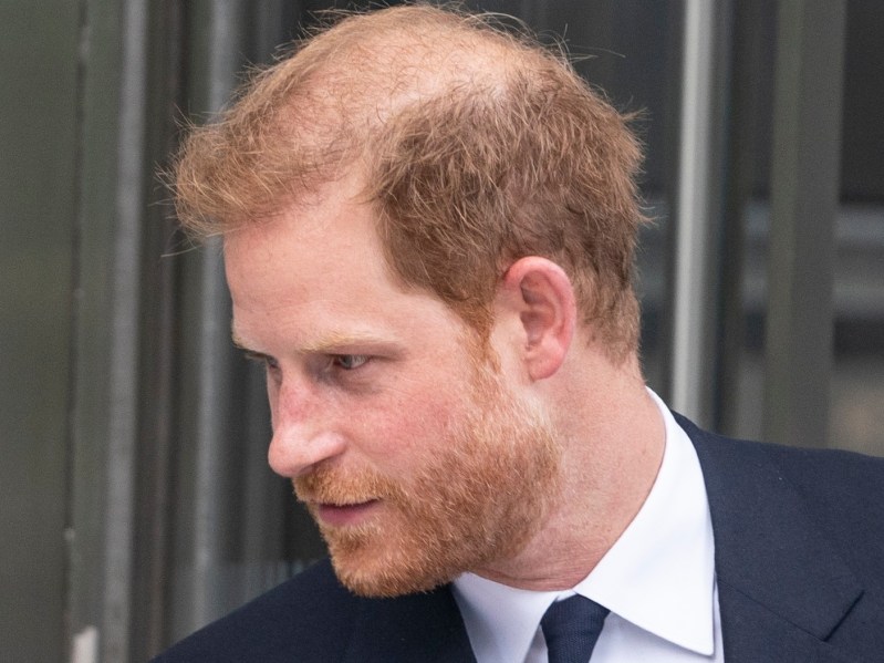Prince Harry wears a black suit while greeting a woman offscreen