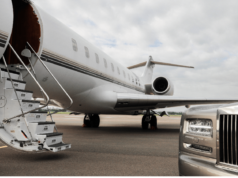 A private jet sits on the tarmac with the stairs down and a luxury car in the foreground