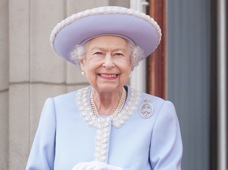 Queen Elizabeth II smiles while wearing periwinkle jacket and matching hat