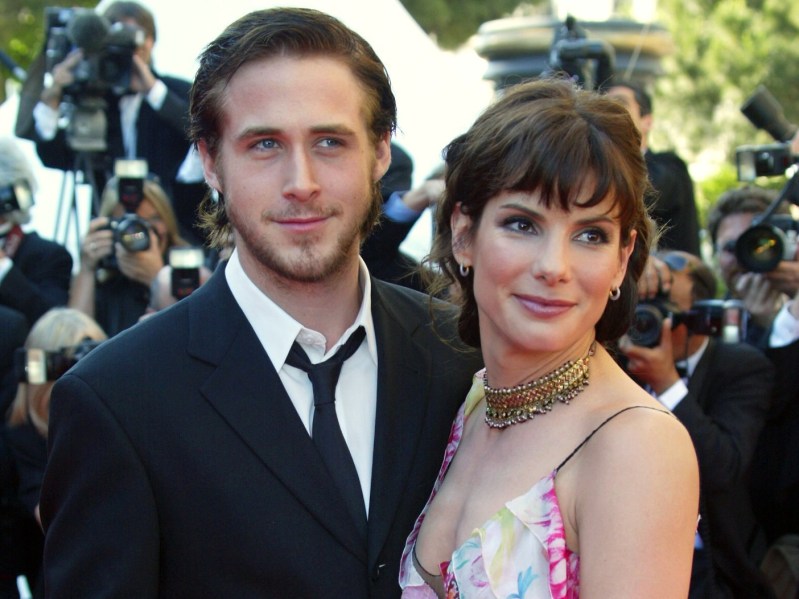 Ryan Gosling (L) in suit and Sranda Bullock in pink patterned dress, both standing outside surrounded by photographers