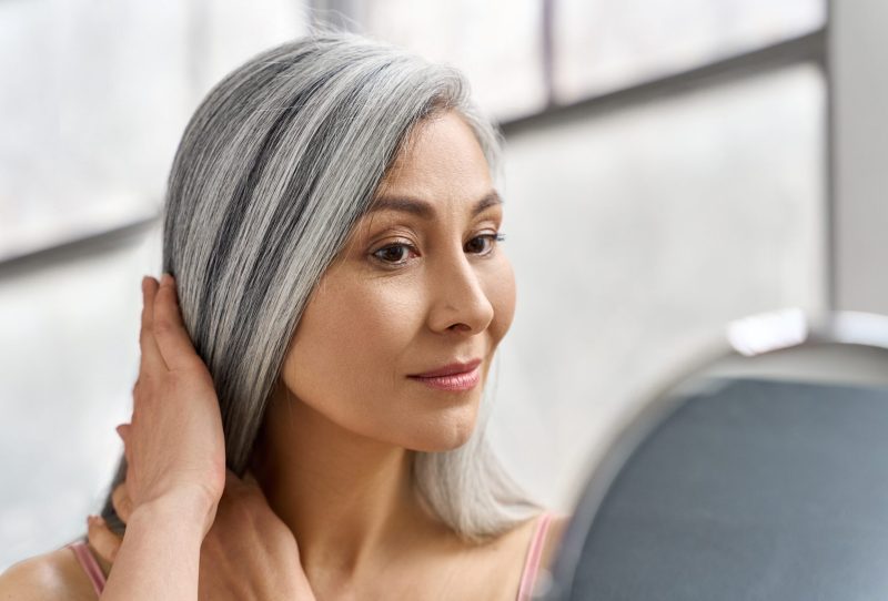 Woman smoothing her gray hair while looking in the mirror