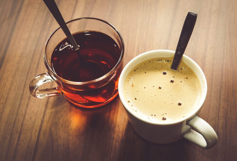 A glass mug of tea and a white mug of coffee on a wooden table