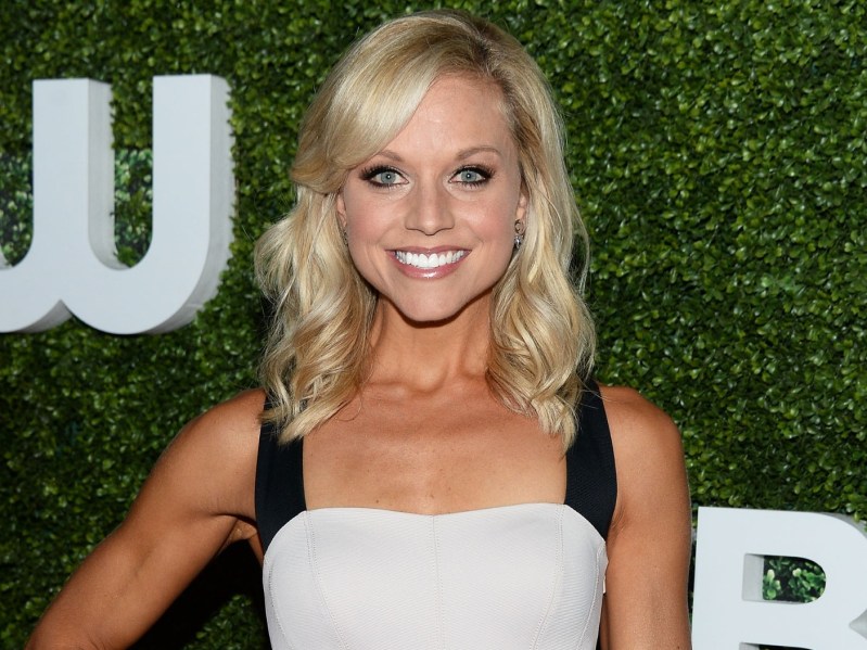 Tiffany Coyne smiles with a hand on her hip, wearing a white dress with thick black straps