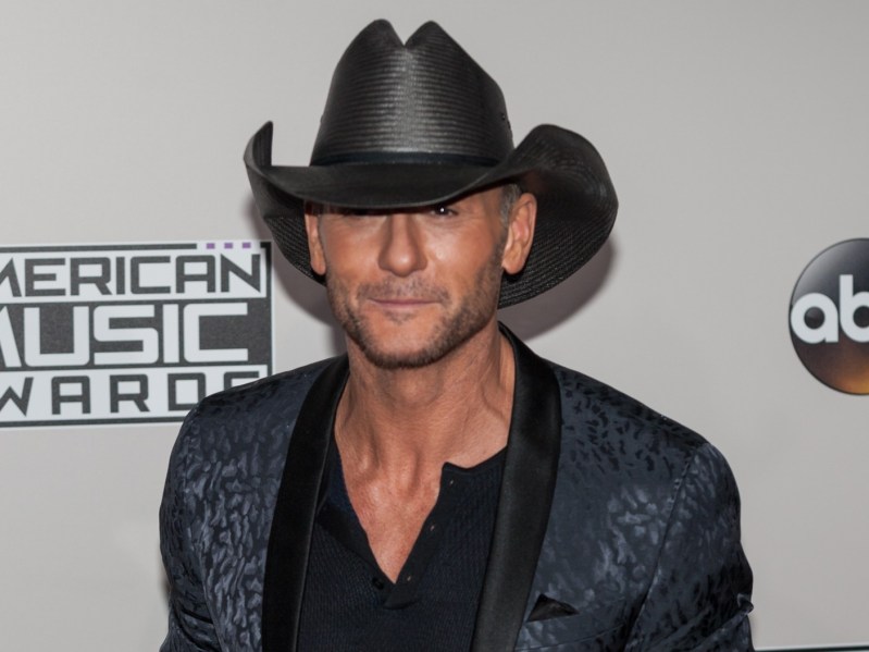 Tim McGraw wearing black outfit with black cowboy hat against white backdrop