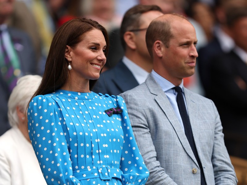 Kate Middleton (L) in blue polka-dotted dress sitting next to Prince William, who is wearing a gray suit jacket
