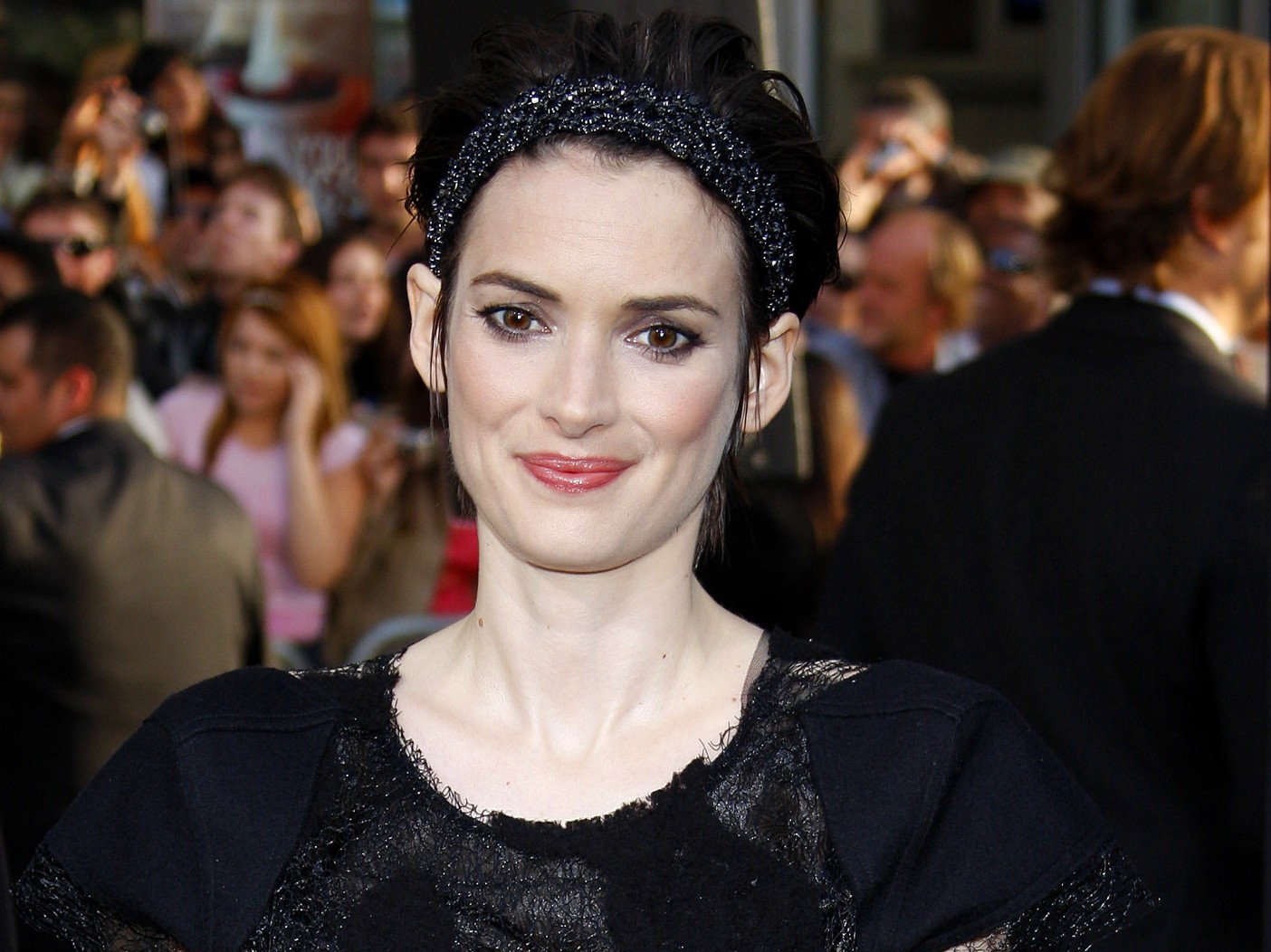 Winona Ryder smiles at a premiere, wearing a black gown and black beaded headband