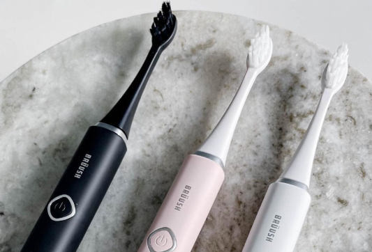 Brüush electric toothbrushes in black, light pink, and white.