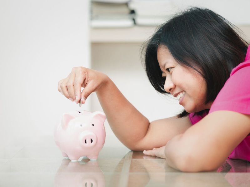 Smiling woman putting coin in piggy bank