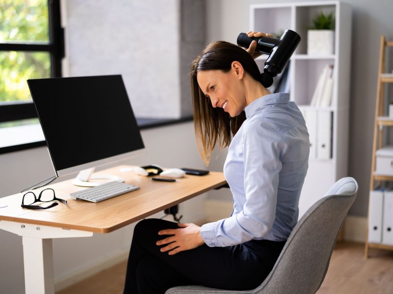 Woman uses massage gun at desk