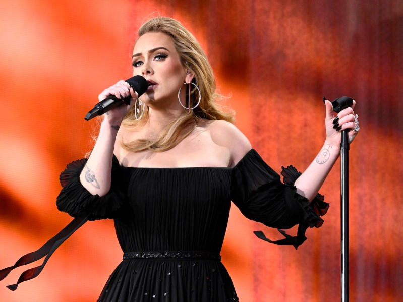 Adele in a black dress singing into a microphone on stage in July 2022