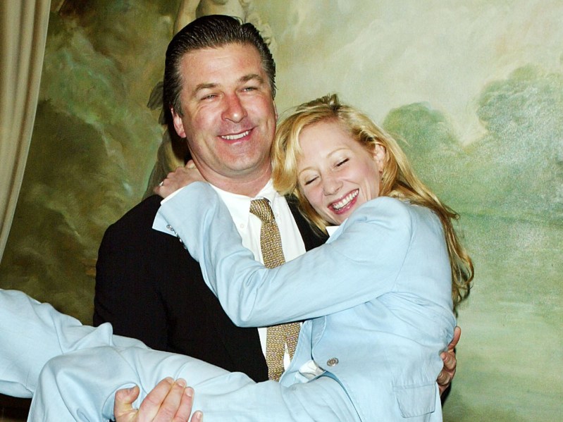 Alec Baldwin in a black suit and gold tie holding Anne Heche, who is dressed in a pale blue pantssuit