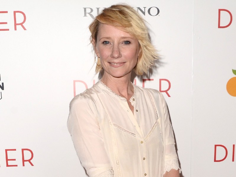 Anne Heche smiling in cream-colored dress against white backdrop