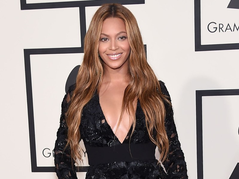 Beyoncé smiling in black dress against white backdrop