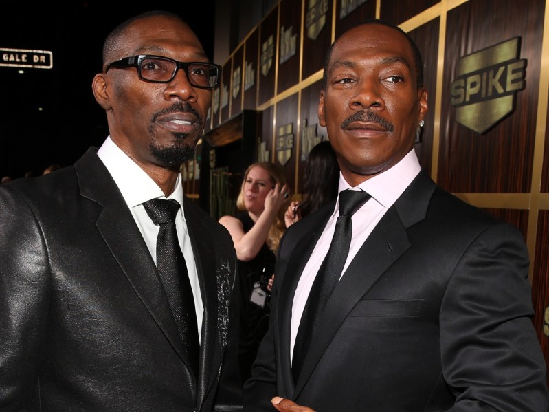 Eddie Murphy (R) in classic black suit and tie standing next to Charlie Murphy, who is dressed the same