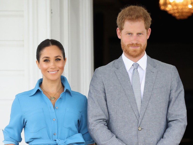 Meghan Markle (L) in blue dress standing next to Prince Harry outside